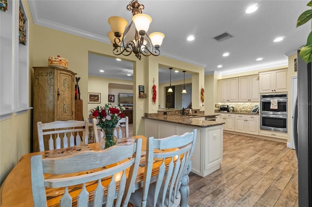 kitchen featuring light wood-type flooring, decorative light fixtures, kitchen peninsula, stainless steel appliances, and a chandelier