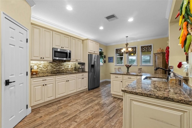 kitchen featuring kitchen peninsula, stainless steel appliances, sink, cream cabinets, and decorative light fixtures