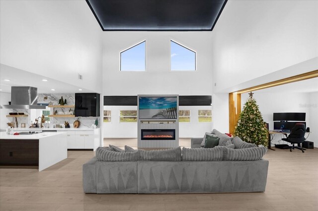 living room with a fireplace, a towering ceiling, light hardwood / wood-style flooring, and sink