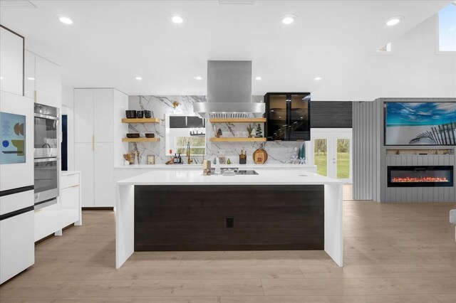 kitchen featuring decorative backsplash, black electric stovetop, island range hood, light hardwood / wood-style flooring, and white cabinets