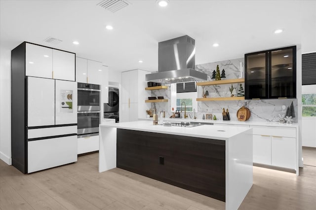 kitchen with decorative backsplash, island range hood, double oven, a healthy amount of sunlight, and stacked washer and clothes dryer