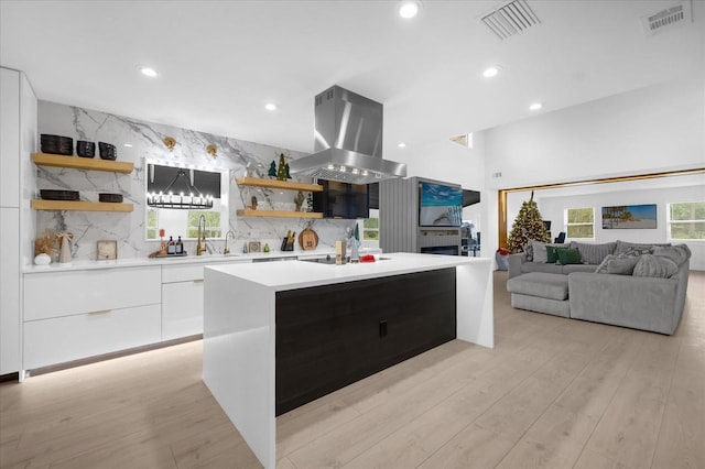 kitchen with a center island with sink, sink, decorative backsplash, island range hood, and white cabinetry