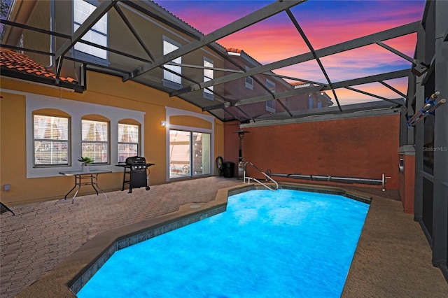 pool at dusk with glass enclosure and a patio area