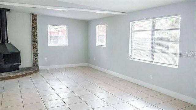 unfurnished living room with light tile patterned floors, a wood stove, and a wealth of natural light