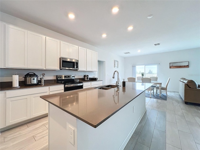 kitchen with a kitchen island with sink, white cabinetry, sink, and appliances with stainless steel finishes