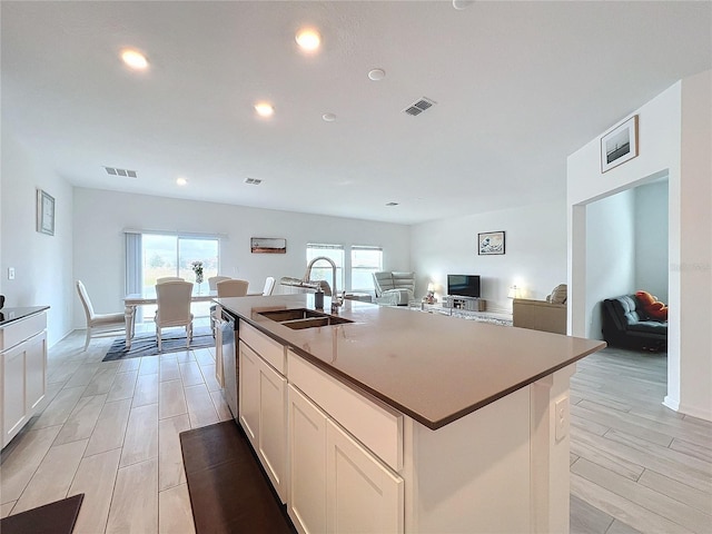 kitchen featuring white cabinetry, dishwasher, sink, light hardwood / wood-style flooring, and an island with sink