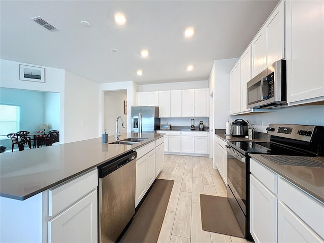 kitchen featuring white cabinets, appliances with stainless steel finishes, a kitchen island with sink, and sink