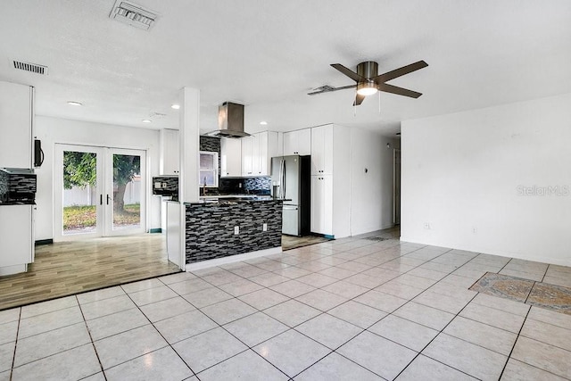 kitchen featuring ceiling fan, wall chimney range hood, white cabinets, stainless steel fridge with ice dispenser, and light tile patterned floors