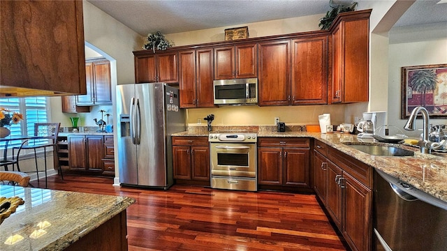 kitchen featuring sink, a textured ceiling, appliances with stainless steel finishes, dark hardwood / wood-style flooring, and light stone counters