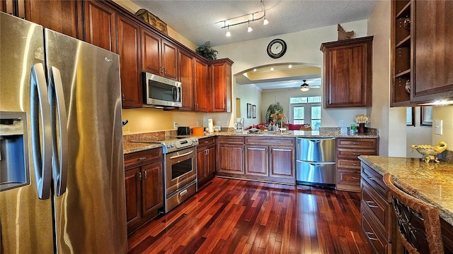 kitchen with ceiling fan, light stone countertops, a textured ceiling, dark hardwood / wood-style flooring, and stainless steel appliances