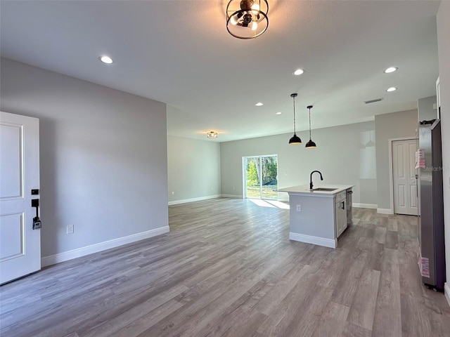 kitchen with sink, decorative light fixtures, a center island with sink, light hardwood / wood-style floors, and white cabinetry