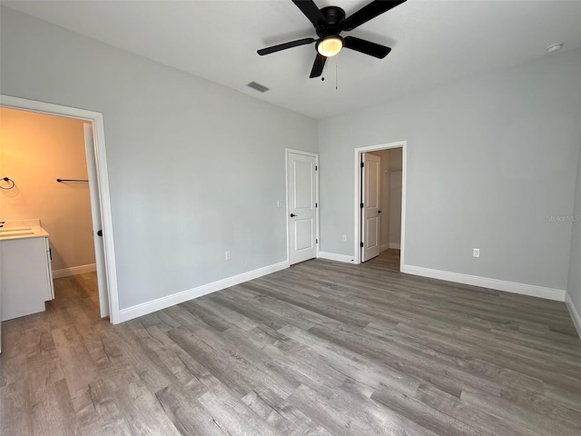 unfurnished bedroom featuring ceiling fan, a walk in closet, light wood-type flooring, and ensuite bath