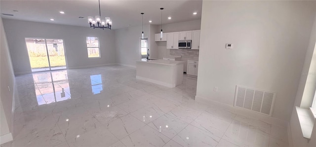 kitchen with a kitchen island with sink, sink, hanging light fixtures, tasteful backsplash, and white cabinetry