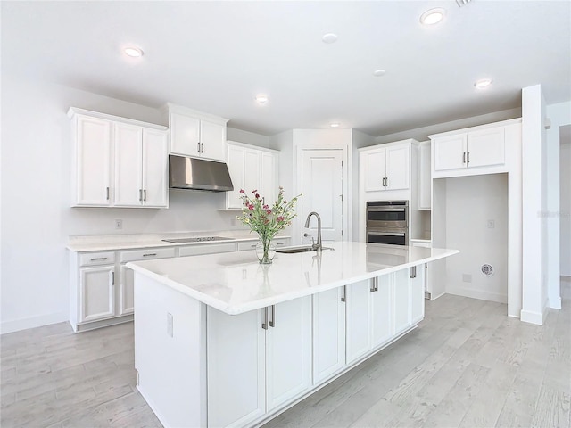 kitchen with a kitchen island with sink, white cabinets, and light hardwood / wood-style floors