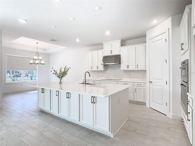 kitchen featuring black electric stovetop, sink, pendant lighting, a center island with sink, and white cabinets