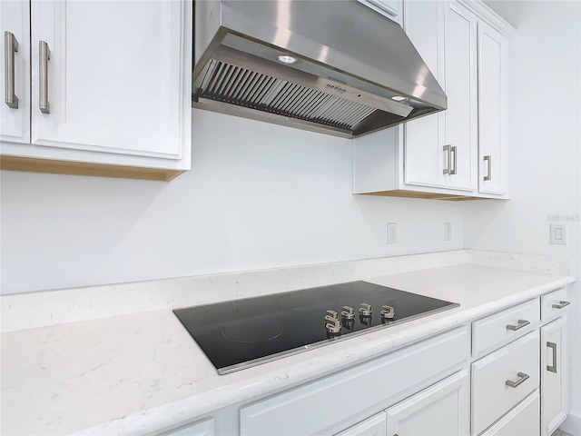 kitchen with black electric stovetop, light stone counters, white cabinetry, and exhaust hood