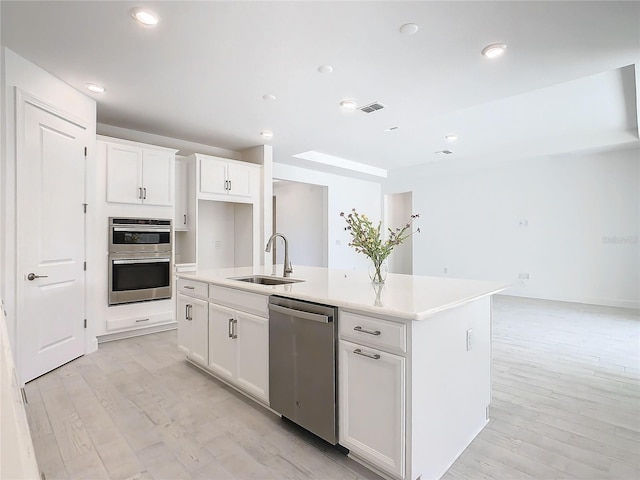 kitchen featuring white cabinetry, sink, light hardwood / wood-style floors, a center island with sink, and appliances with stainless steel finishes