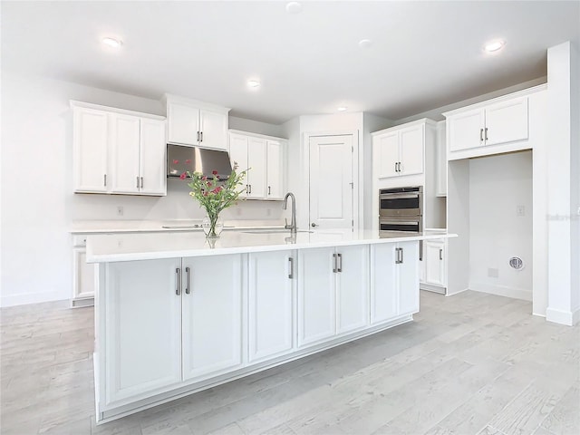 kitchen featuring white cabinets, light wood-type flooring, and a center island with sink