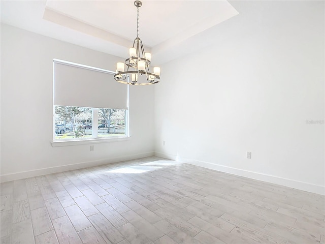 empty room featuring a chandelier, light wood-type flooring, and a tray ceiling