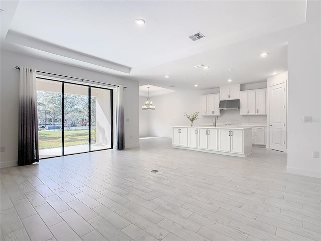 unfurnished living room with sink, a chandelier, and light hardwood / wood-style floors