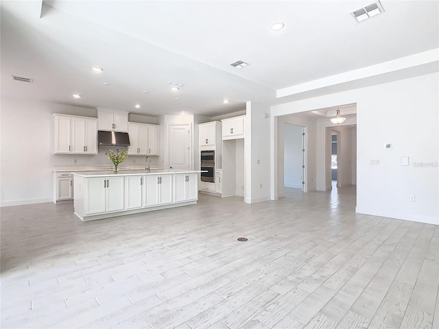 kitchen featuring sink, double oven, light hardwood / wood-style floors, a kitchen island with sink, and white cabinets