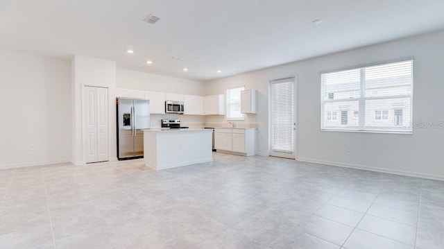 kitchen with white cabinets, appliances with stainless steel finishes, a kitchen island, and a healthy amount of sunlight