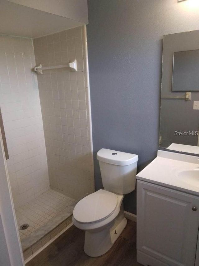 bathroom featuring a tile shower, vanity, hardwood / wood-style flooring, and toilet