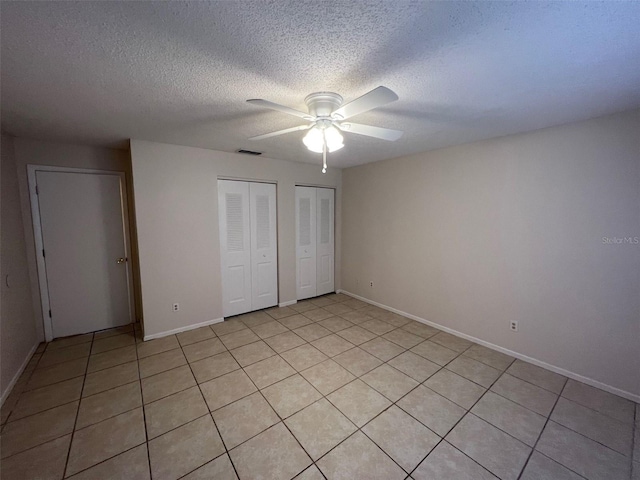 unfurnished bedroom featuring ceiling fan, light tile patterned floors, a textured ceiling, and multiple closets