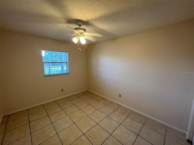 empty room with ceiling fan, light tile patterned flooring, and a textured ceiling