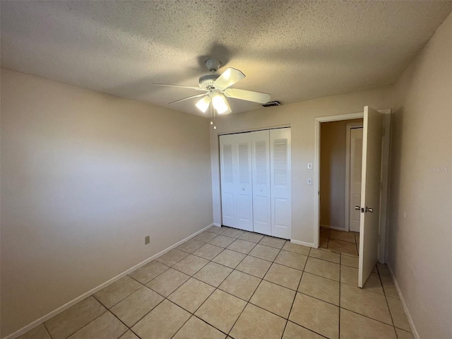 unfurnished bedroom featuring ceiling fan, a closet, light tile patterned floors, and a textured ceiling