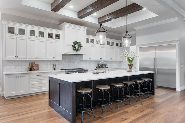 kitchen with beam ceiling, an island with sink, light hardwood / wood-style floors, decorative backsplash, and white cabinets