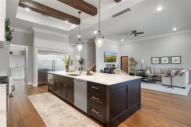 kitchen with stainless steel appliances, sink, wood-type flooring, pendant lighting, and a center island with sink