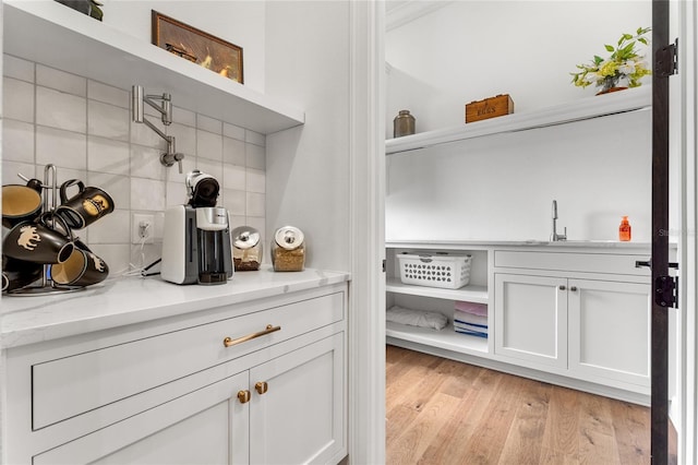 bar featuring sink, light stone countertops, light wood-type flooring, tasteful backsplash, and white cabinetry