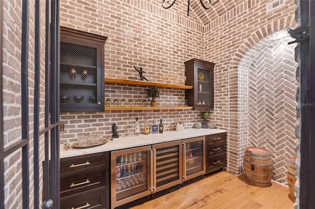 bar featuring dark brown cabinets, light wood-type flooring, and brick wall