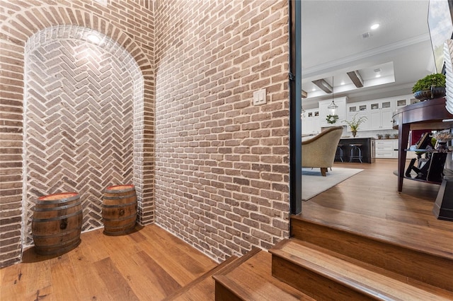 wine cellar featuring beam ceiling, hardwood / wood-style flooring, ornamental molding, and brick wall