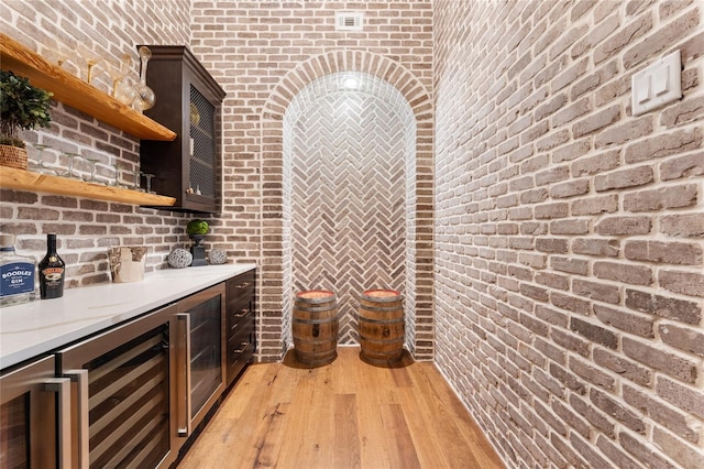 bar with dark brown cabinetry, beverage cooler, and brick wall