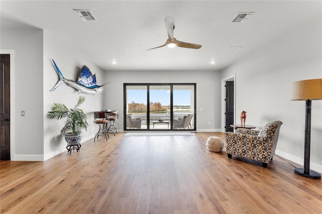 living area featuring ceiling fan, light wood-type flooring, and a textured ceiling