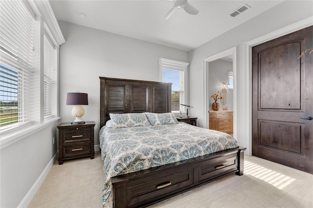 carpeted bedroom featuring multiple windows, ensuite bath, and ceiling fan