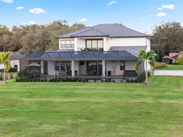 rear view of property with glass enclosure, a patio area, and a yard