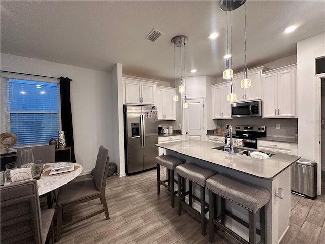 kitchen featuring white cabinetry, stainless steel appliances, light hardwood / wood-style flooring, pendant lighting, and a kitchen island with sink