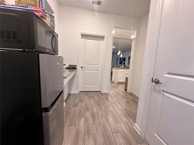 kitchen with black refrigerator, white cabinets, and light hardwood / wood-style floors