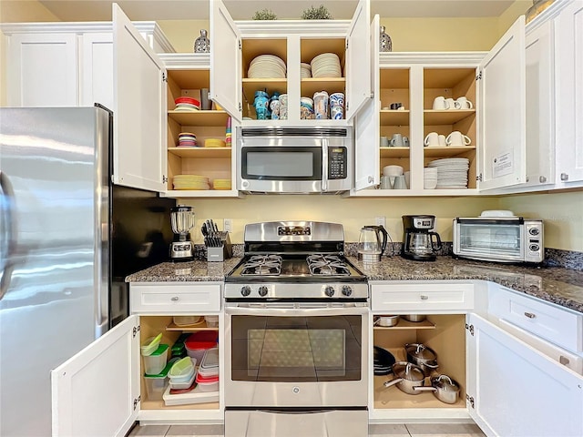 kitchen with white cabinets, light tile patterned floors, stainless steel appliances, and dark stone countertops