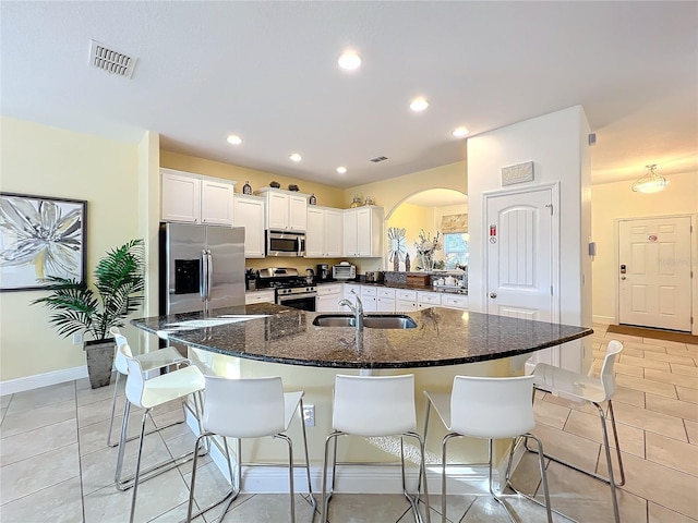 kitchen featuring white cabinetry, sink, stainless steel appliances, a kitchen breakfast bar, and dark stone countertops