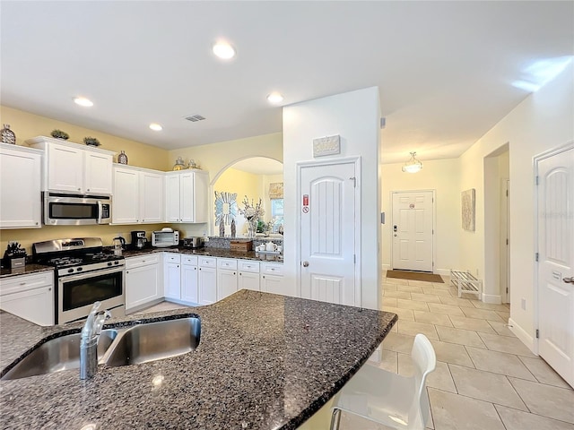 kitchen featuring appliances with stainless steel finishes, dark stone counters, sink, light tile patterned floors, and white cabinetry