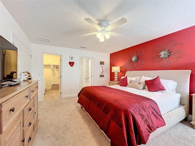 bedroom featuring light carpet, ceiling fan, a spacious closet, a textured ceiling, and a closet