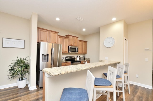 kitchen with light stone counters, a kitchen bar, stainless steel appliances, and dark wood-type flooring