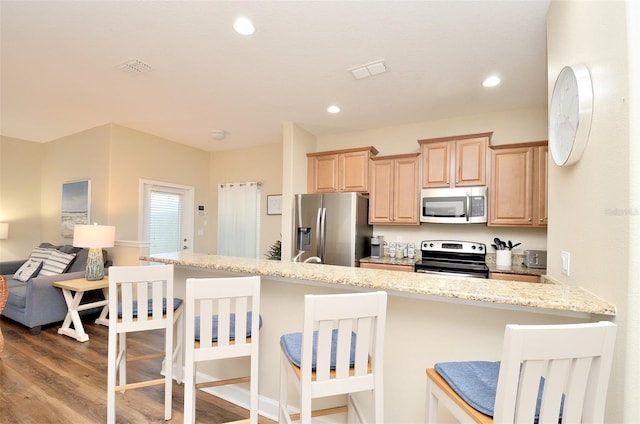 kitchen with light stone countertops, a kitchen breakfast bar, light brown cabinetry, appliances with stainless steel finishes, and light wood-type flooring