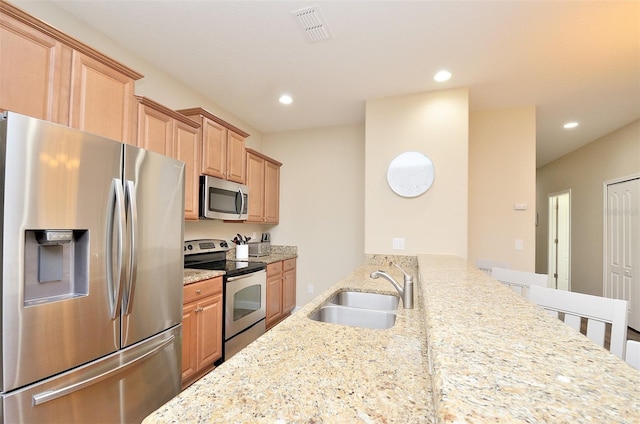 kitchen with kitchen peninsula, sink, light stone countertops, and stainless steel appliances