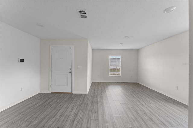 spare room featuring a textured ceiling and light hardwood / wood-style floors