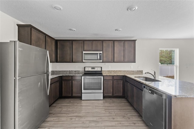 kitchen with kitchen peninsula, appliances with stainless steel finishes, light wood-type flooring, a textured ceiling, and sink